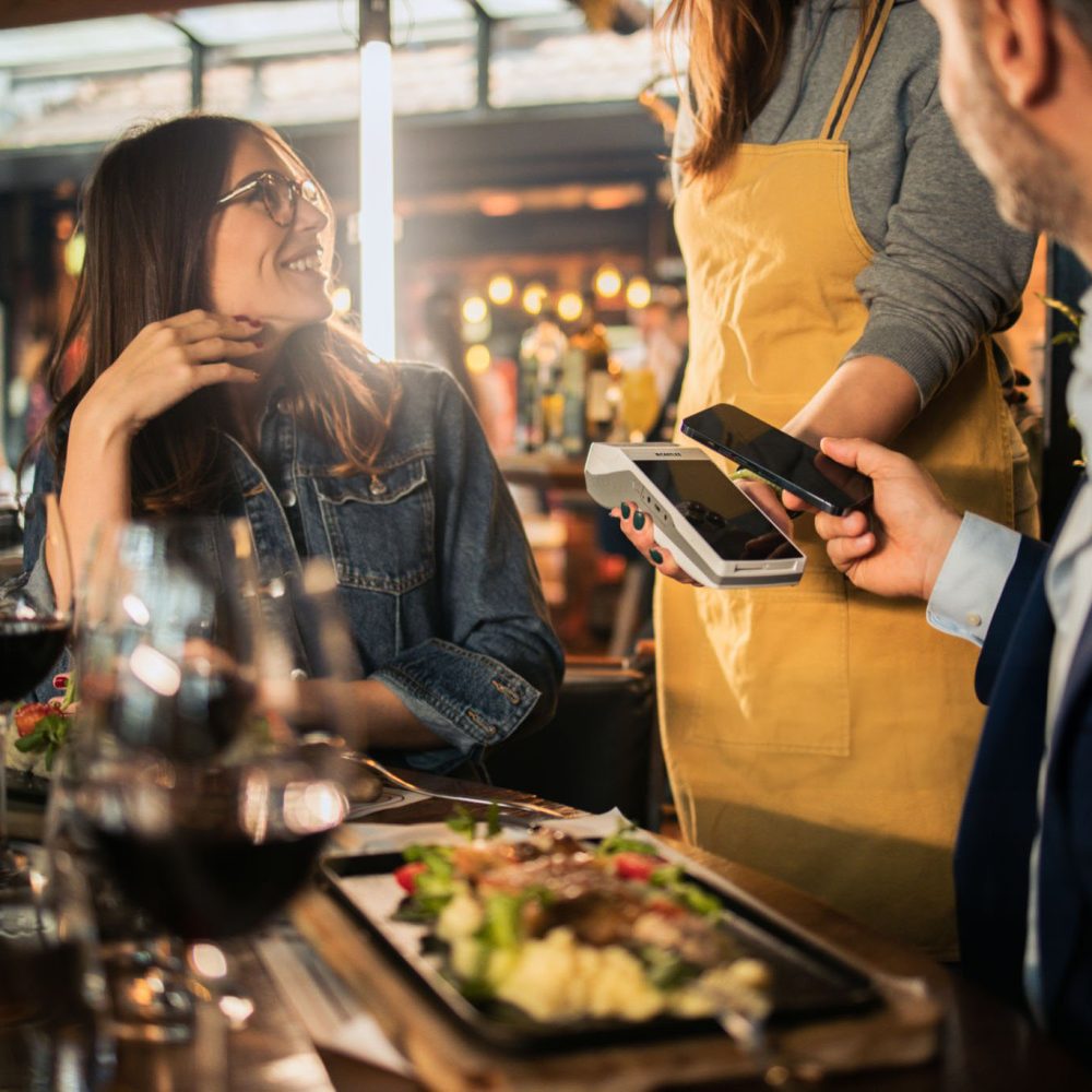 Businessman on a business lunch with clients paying to a waitress at the restaurant.